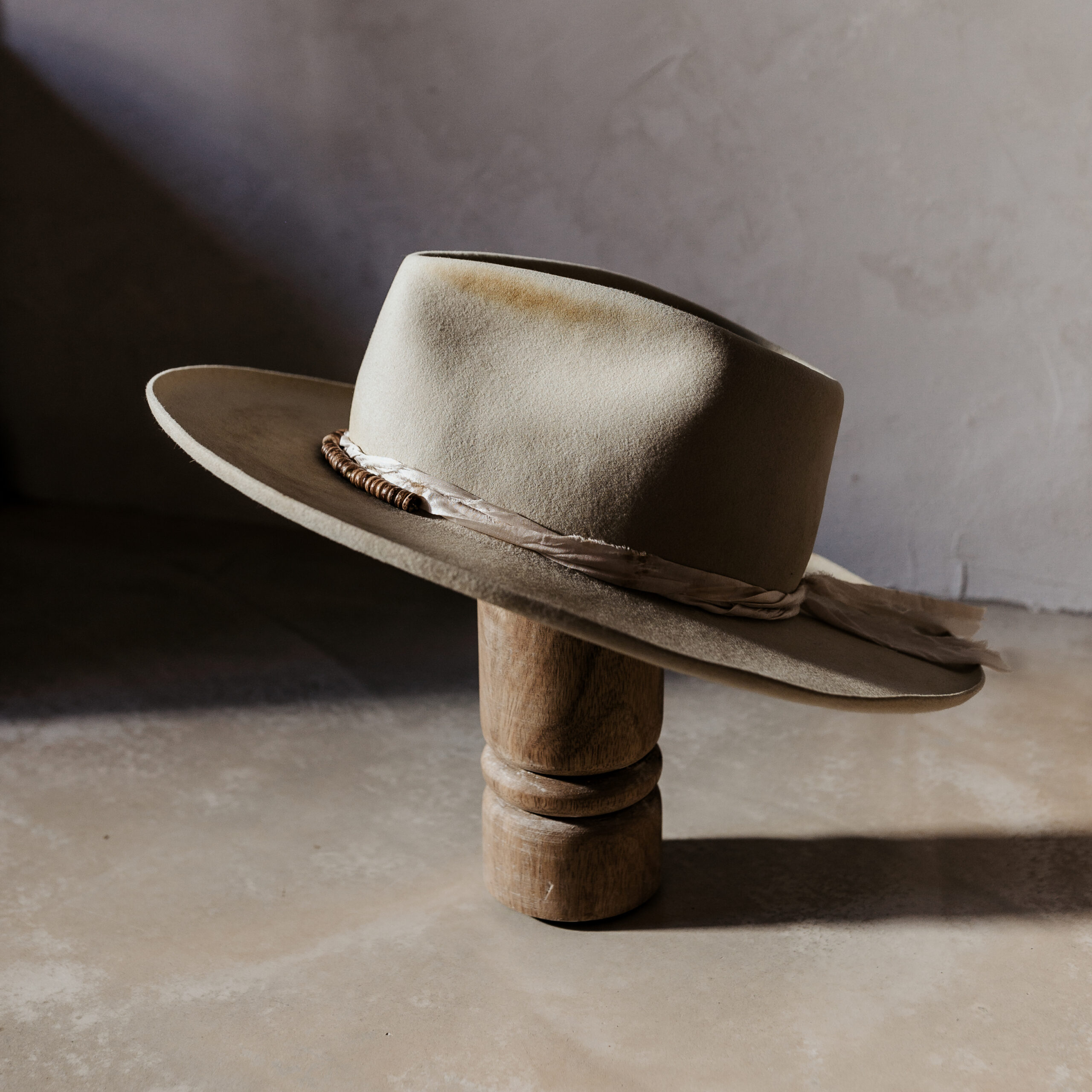 A beautifully handcrafted Crown of the Vagabond hat by the hatters Ruth and Chris on Mallorca with traditional tools in the color Vanilla shaped in Gold Digger with a naturally distressed design consisting of a silk cord tied in the back as well as wood pearls threaded in the front and burn marks on the crown with a curled brim - branded with the serial number 19 made during our image video.