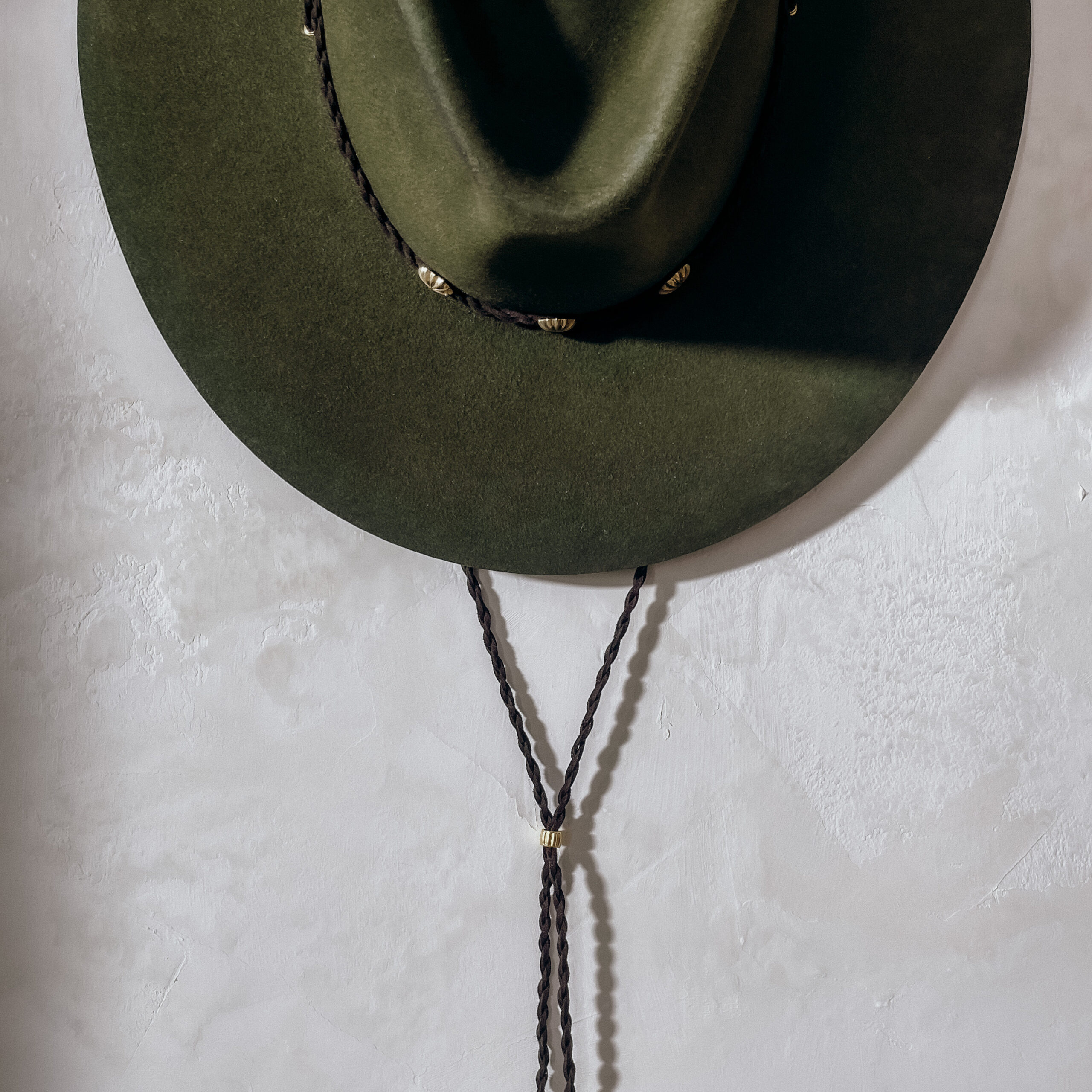 A beautifully handcrafted Crown of the Vagabond hat by the hatters Ruth and Chris on Mallorca with traditional tools in the color Sequoia shaped in Gold Digger and a pinch in the front with a clean simple look inspired by the Spanish horse back riding style consisting of a corded leather string also used as a chinstrap fixed with a golden pearl and golden rivets in the front of the crown and a clean flat brim - branded with the serial number 21.