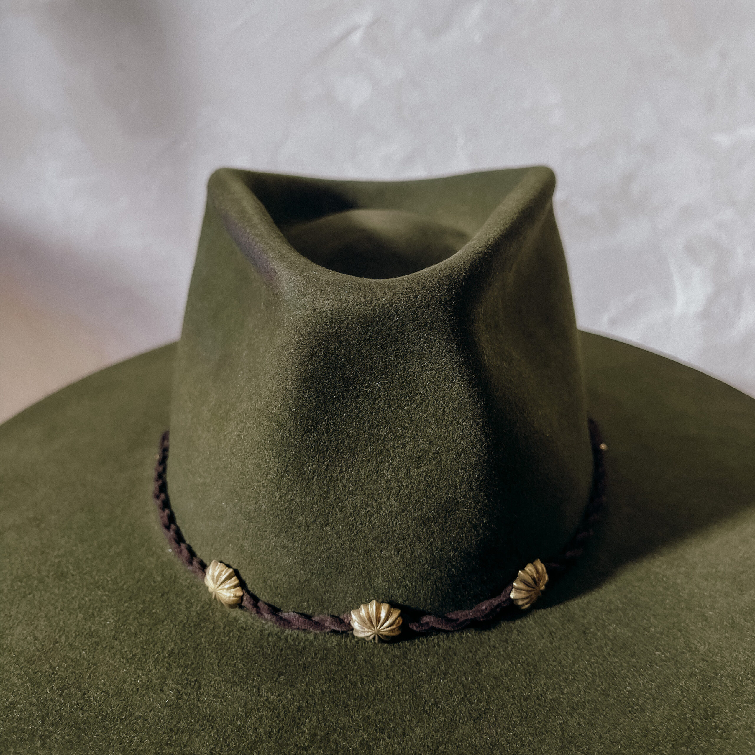 A beautifully handcrafted Crown of the Vagabond hat by the hatters Ruth and Chris on Mallorca with traditional tools in the color Sequoia shaped in Gold Digger and a pinch in the front with a clean simple look inspired by the Spanish horse back riding style consisting of a corded leather string also used as a chinstrap fixed with a golden pearl and golden rivets in the front of the crown and a clean flat brim - branded with the serial number 21.