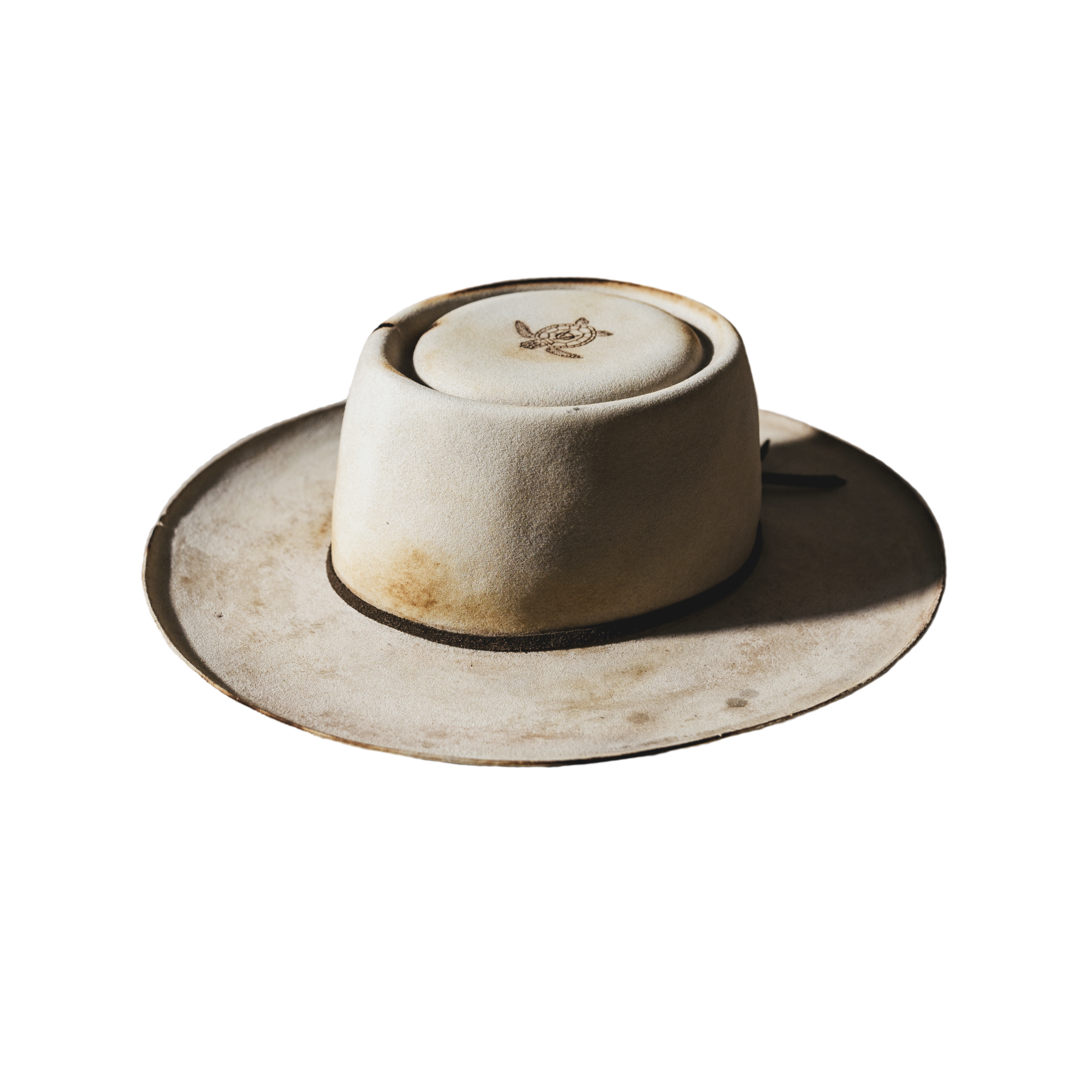 A beautifully handcrafted Crown of the Vagabond hat by the hatters Ruth and Chris on Mallorca with traditional tools in the color Vanilla shaped in Oasis with a distressed used look consisting of burn marks as well as cutouts tied on the crown with a rough leather string fixed with a bronze pearl in the back and a turtle engraved on the top of the crown and a curled brim - branded with the serial number 22.