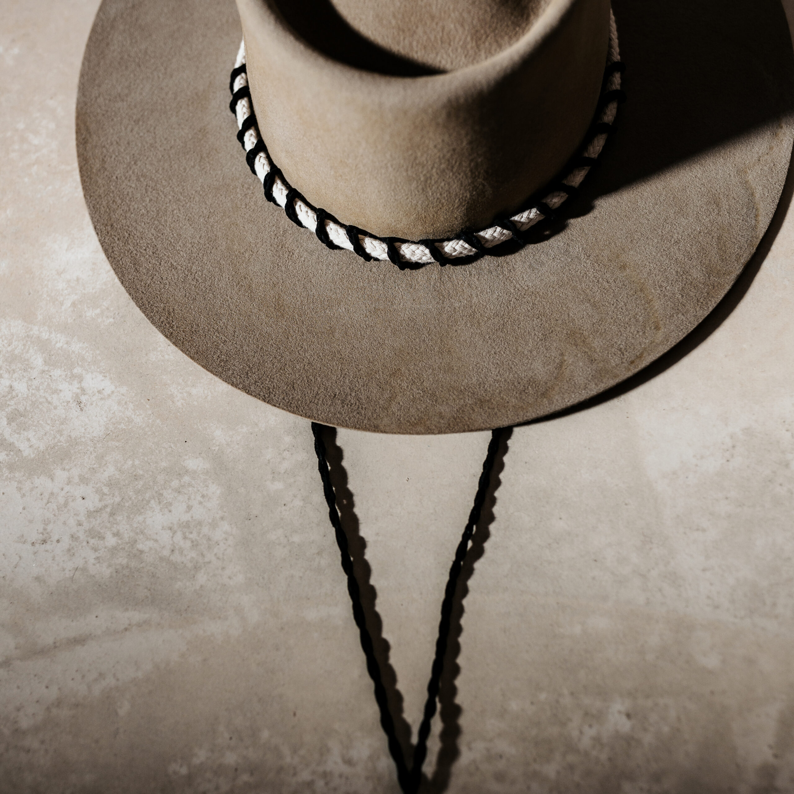 Crown of the Vagabond customised handcrafted hat by Ruth and Chris with traditional tools made in Mallorca, Porto Cristo. Oasis shaped in Prairie Dust with a flat brim in a simple greek style with a white robe surrounded by a black corded leather string which is also used as the chinstrap fixed with a wooden pearl.