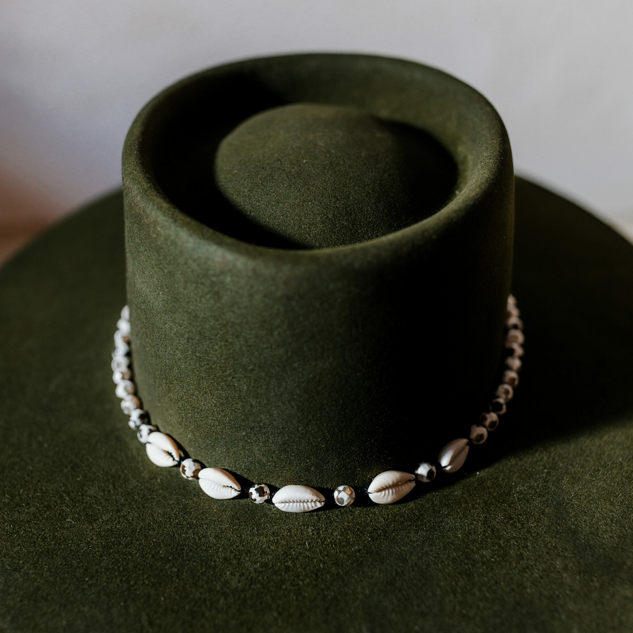 A beautifully handcrafted Crown of the Vagabond hat by the hatters Ruth and Chris on Mallorca with traditional tools in the color Sequoia shaped in Oasis with a clean simple look consisting of edged black-white pearls separated by small black beets and shells in the front with a clean flat brim - branded with the serial number 25.