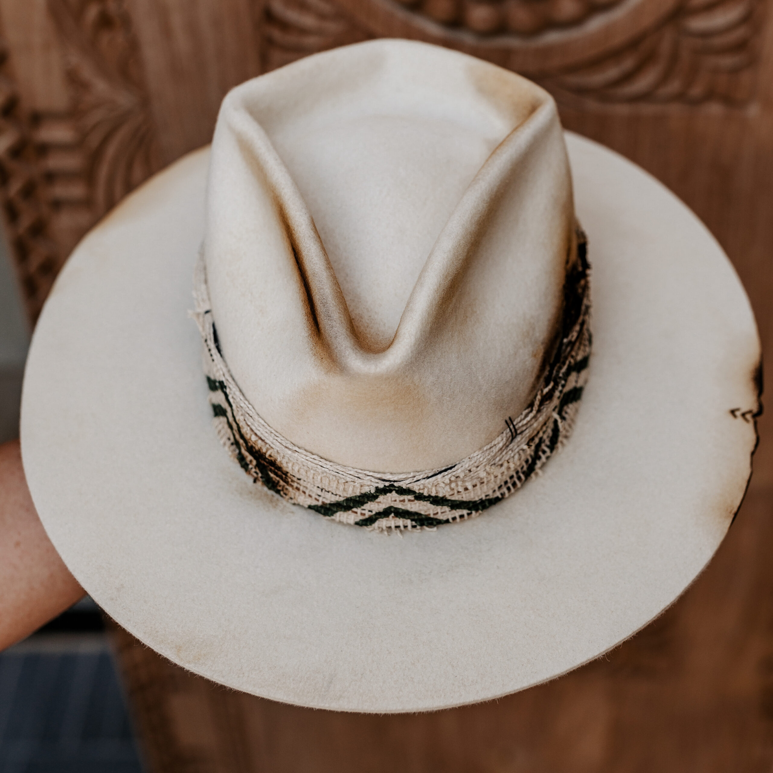 A beautifully handcrafted Crown of the Vagabond hat by the hatters Ruth and Chris on Mallorca with traditional tools in the color Snow shaped in Stargazer with a rough adventurer look mostly distressed consisting of a woven thick headband with stitches on crown and band as well as custom laser branding on crown and brim near the cutouts. The flat brim has cutouts as well as burn marks all over and the sweatband wears the number 28.