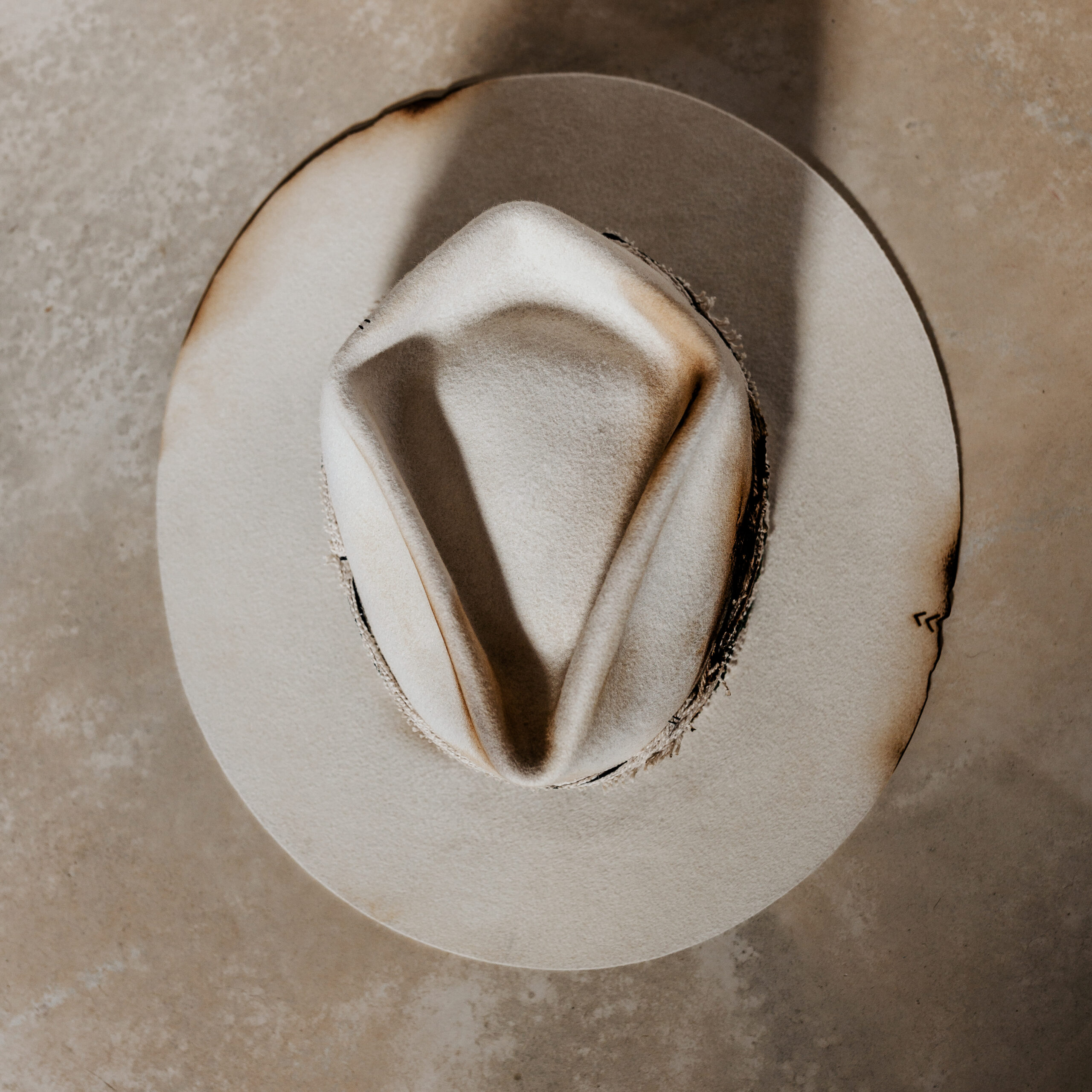 A beautifully handcrafted Crown of the Vagabond hat by the hatters Ruth and Chris on Mallorca with traditional tools in the color Snow shaped in Stargazer with a rough adventurer look mostly distressed consisting of a woven thick headband with stitches on crown and band as well as custom laser branding on crown and brim near the cutouts. The flat brim has cutouts as well as burn marks all over and the sweatband wears the number 28.