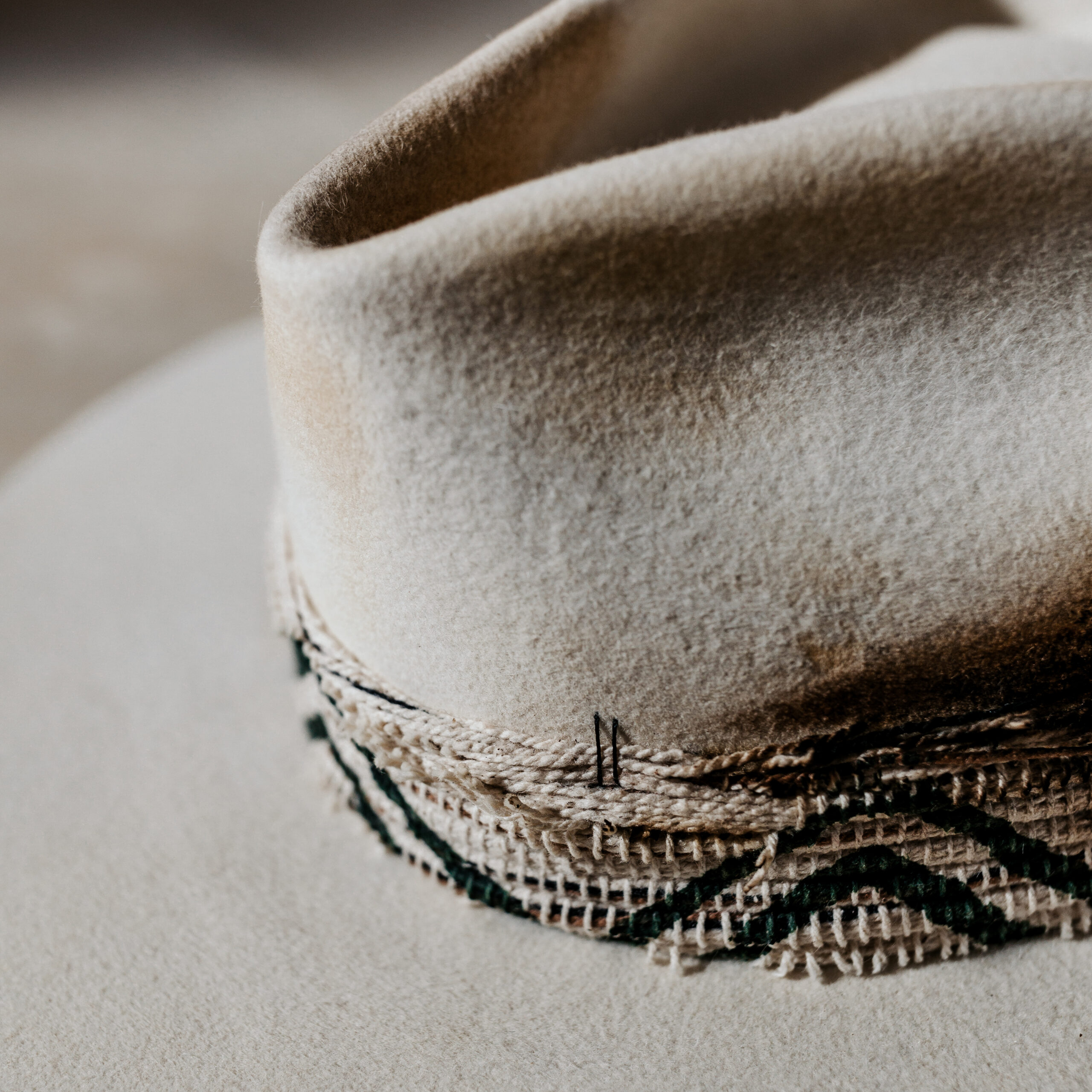 A beautifully handcrafted Crown of the Vagabond hat by the hatters Ruth and Chris on Mallorca with traditional tools in the color Snow shaped in Stargazer with a rough adventurer look mostly distressed consisting of a woven thick headband with stitches on crown and band as well as custom laser branding on crown and brim near the cutouts. The flat brim has cutouts as well as burn marks all over and the sweatband wears the number 28.