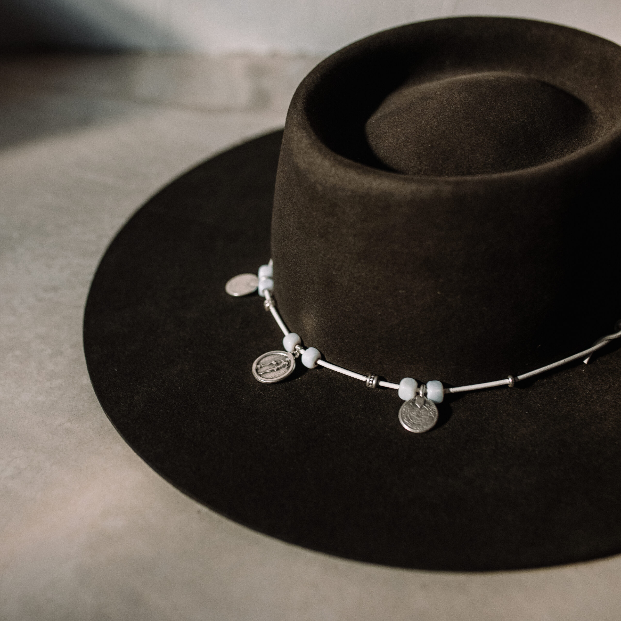 Crown of the Vagabond Hat on Mallorca in color Tortuga Oasis-shaped. Centred silver Coins on a white leather string.