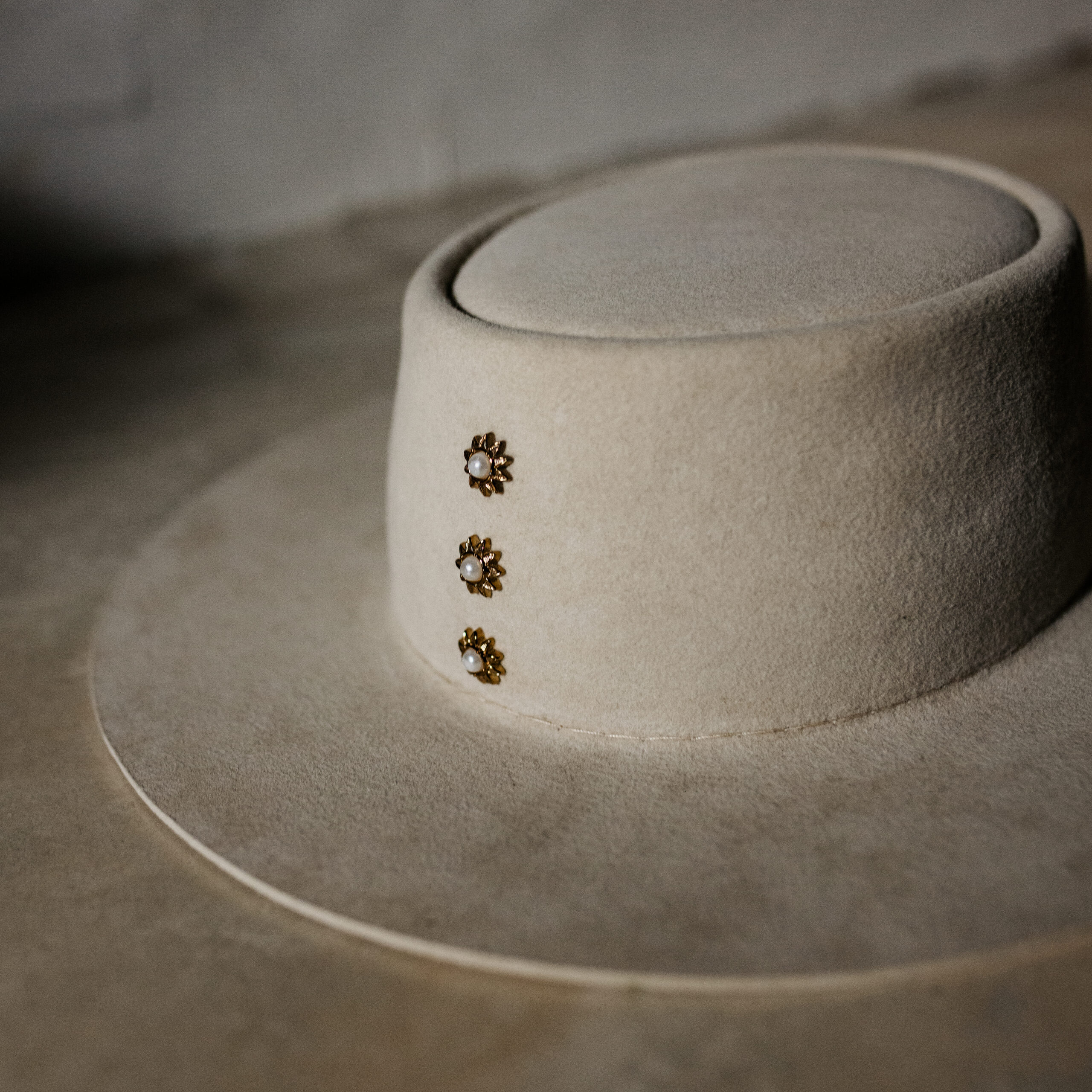 Crown of the Vagabond hat on Mallorca in color Bone Oasis-shaped. Centred golden pearl rivets and a clean flat 8cm / 3.14in brim.