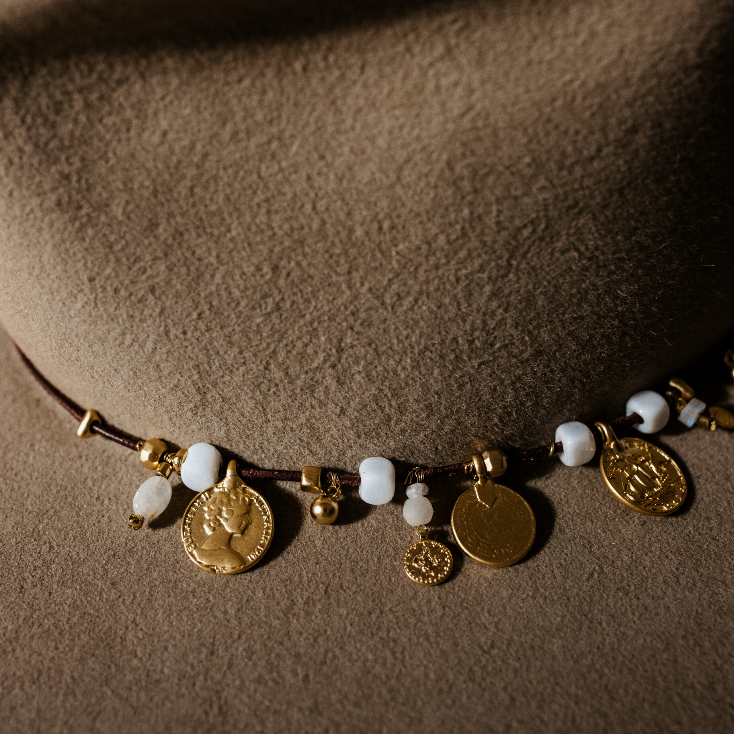 Crown of the Vagabond hat on Mallorca in color Prairie Dust Gold-Digger-shaped. Off centred golden coins and pearls on leather strand.