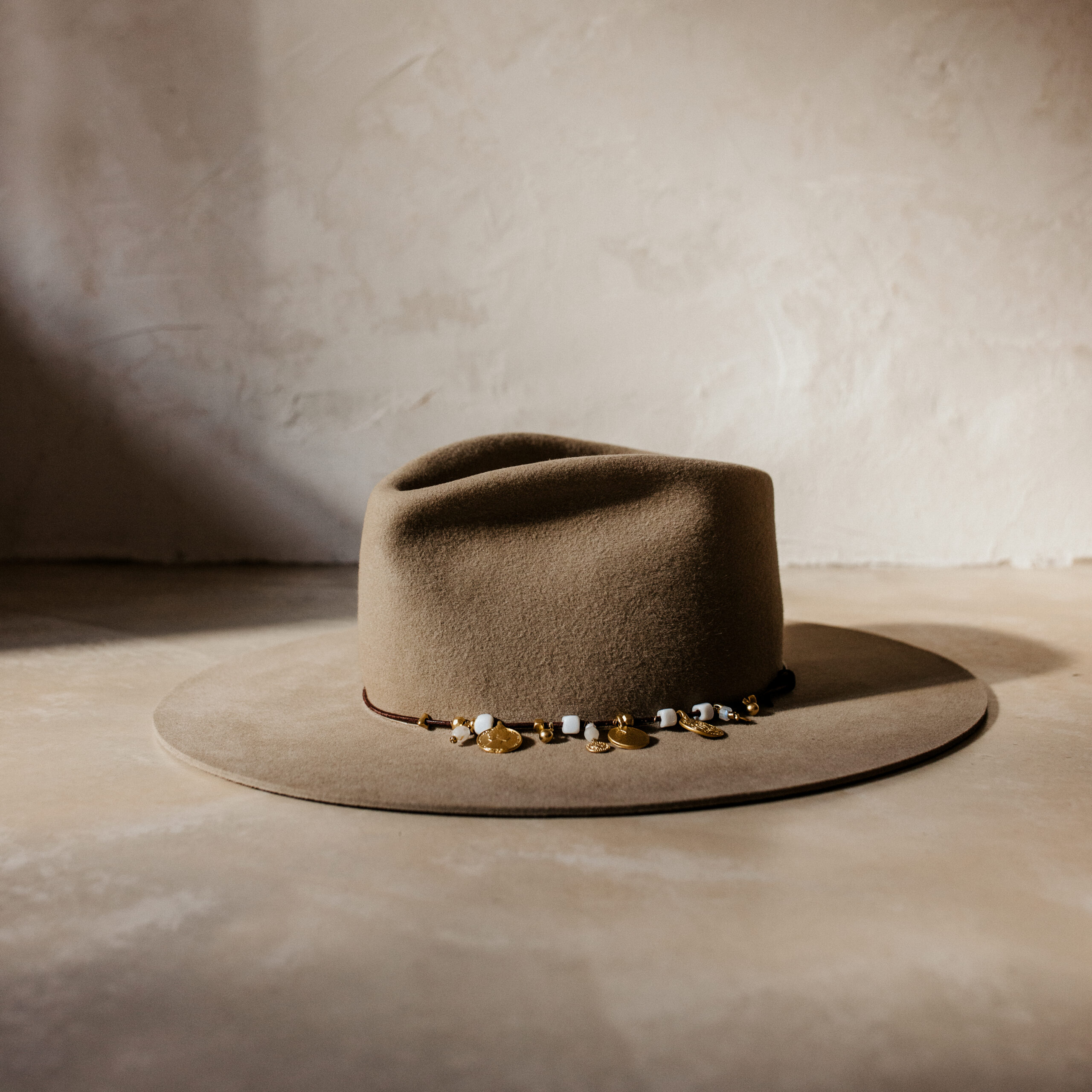 Crown of the Vagabond hat on Mallorca in color Prairie Dust Gold-Digger-shaped. Off centred golden coins and pearls on leather strand.